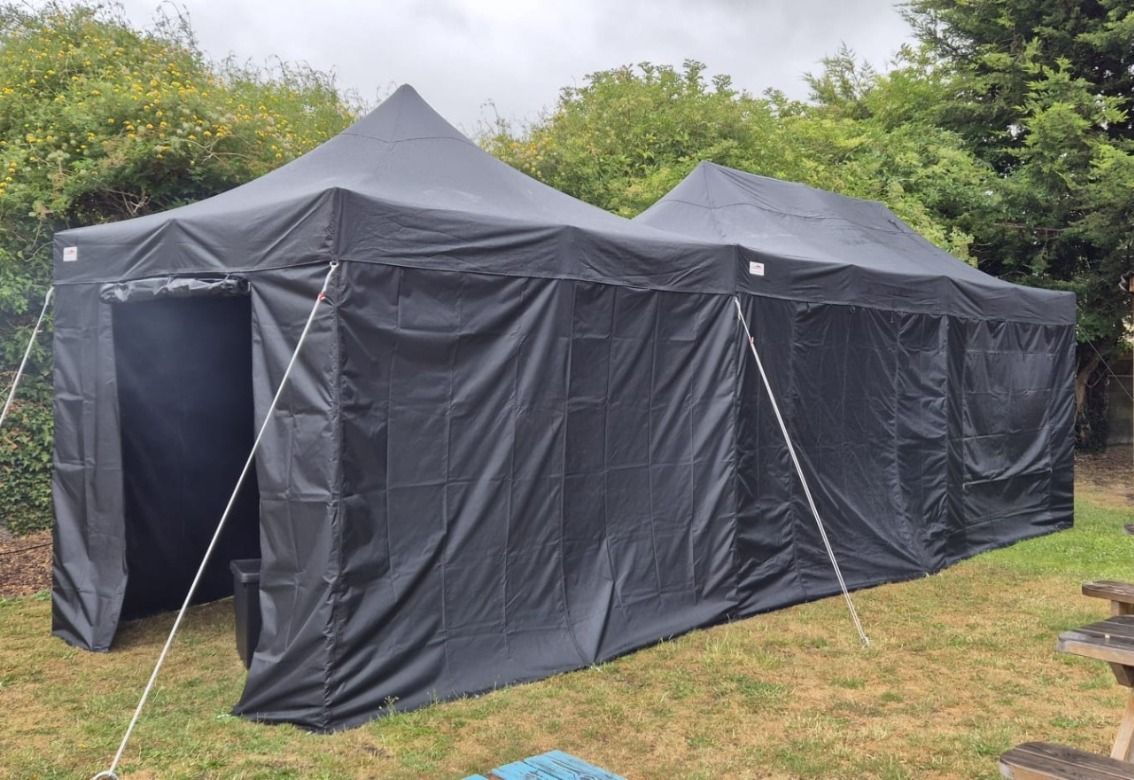Large black canopy tent set up on grass outdoors under overcast skies