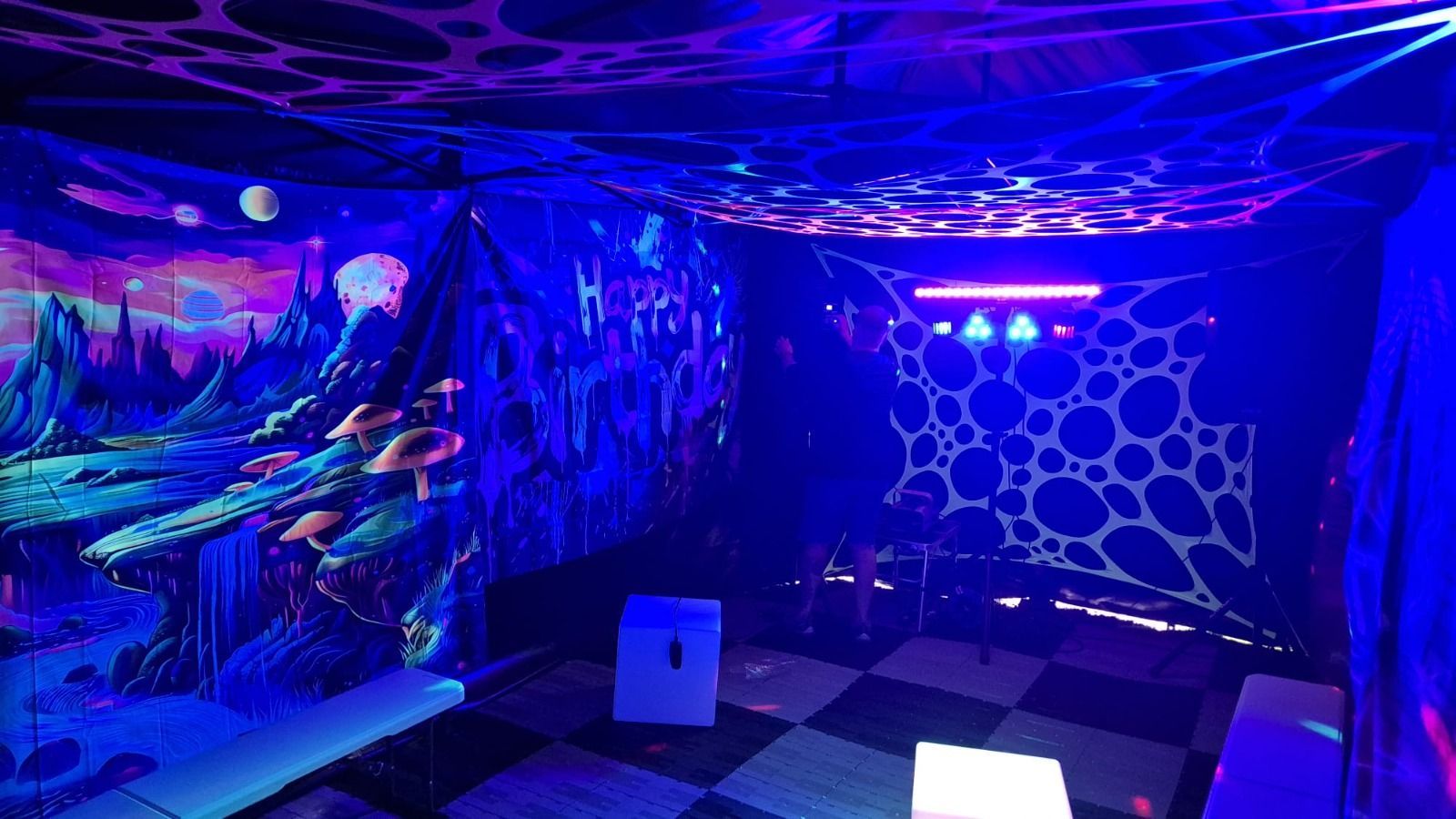 Neon-blue room with abstract wall art, honeycomb pattern, and low benches under UV lighting