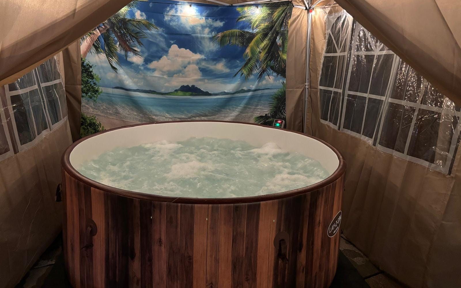 Round wooden hot tub in a tented room with tropical mural and string lights