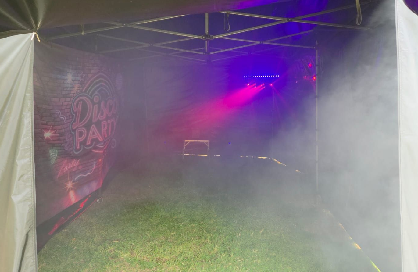 Foggy tent interior with purple lights and a graffiti-style wall over grass flooring