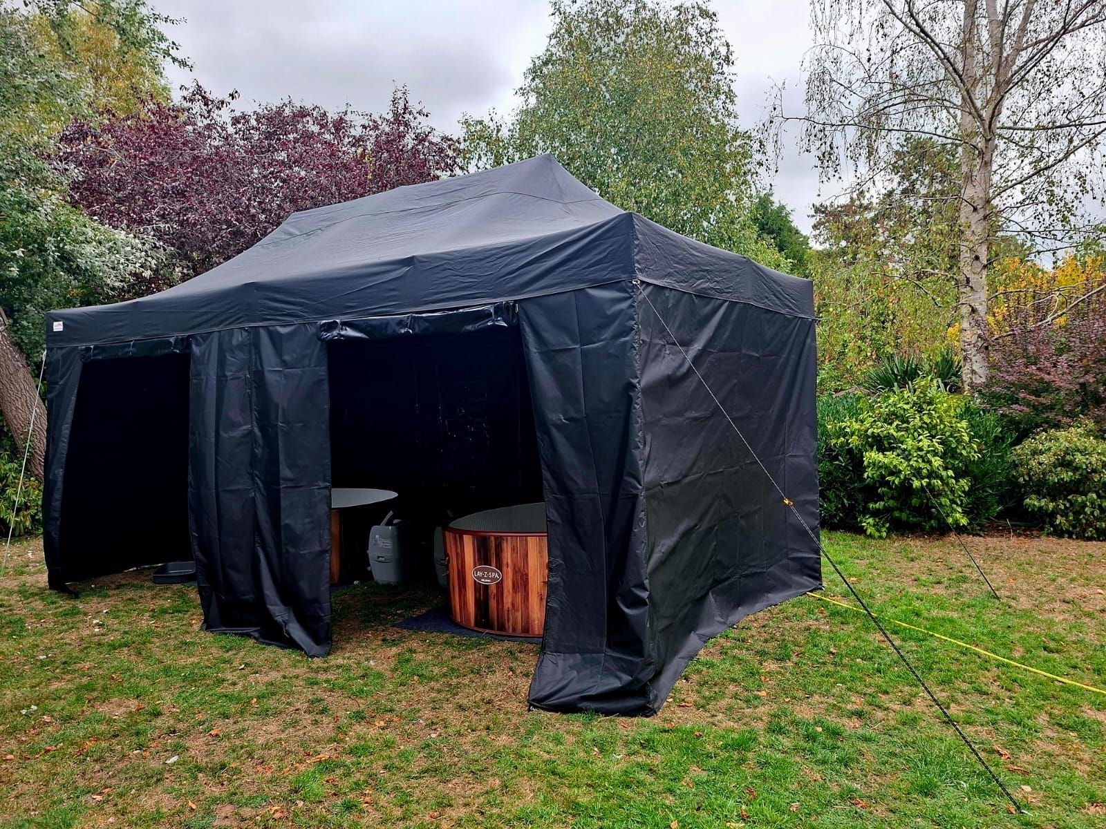 Black canopy tent set up on grass in a backyard, with wooden stools inside.