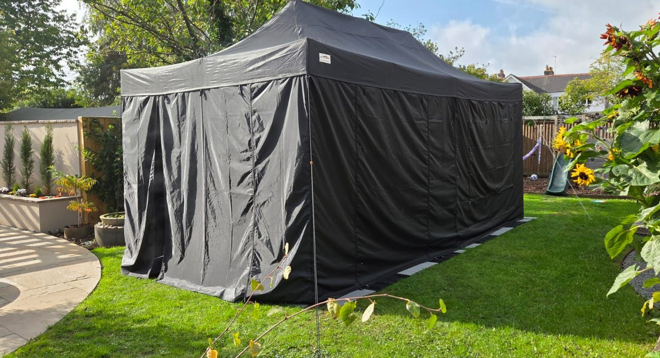 Black canopy tent on a grassy backyard lawn beside a patio and garden