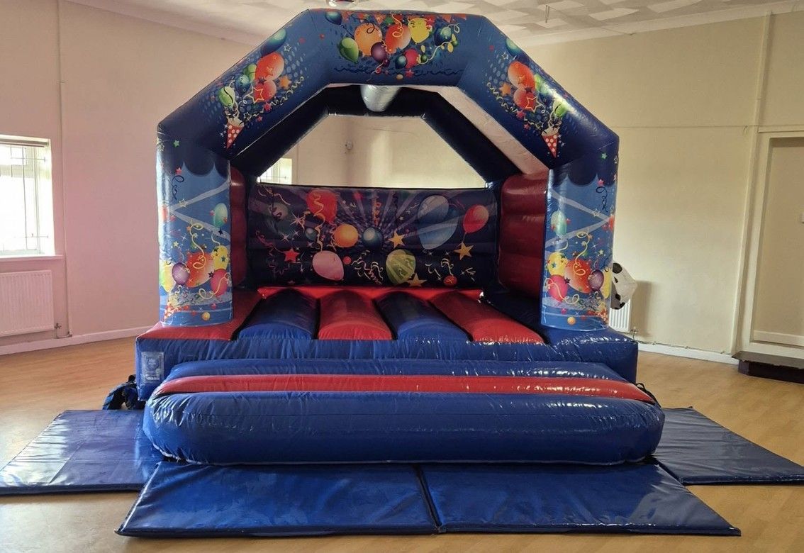 Colorful inflatable bounce house with slide set up indoors on a blue tarp in a room.