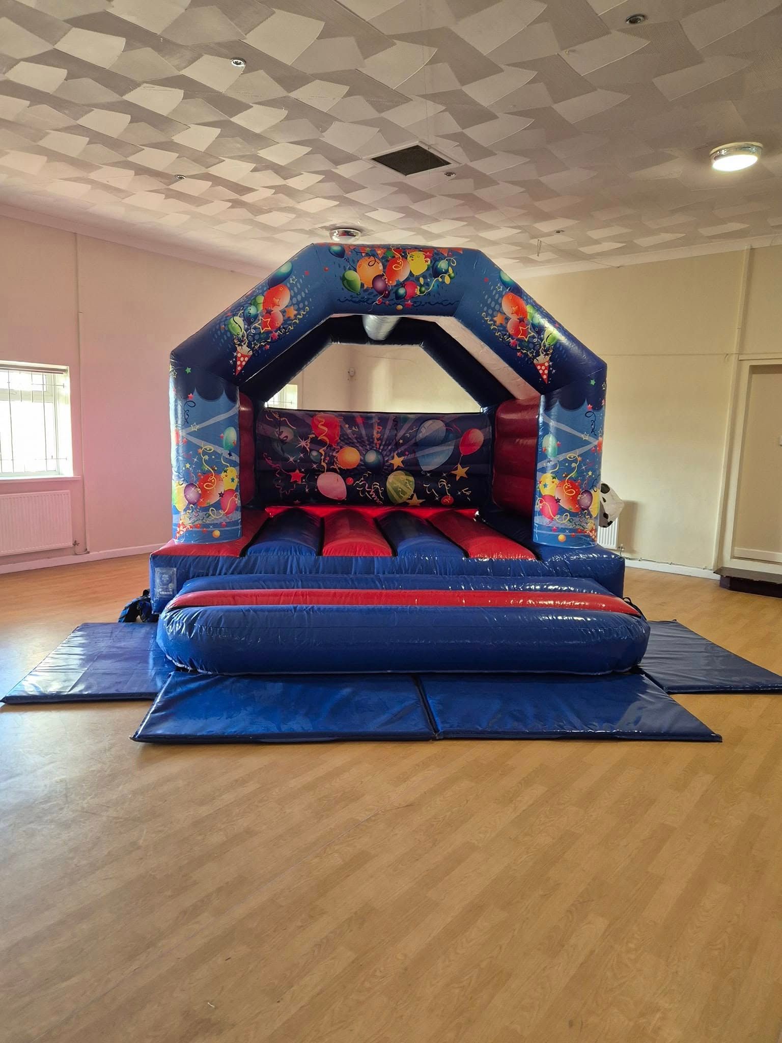 Colorful inflatable bounce house with slide in a large indoor hall with wood floors and pink walls