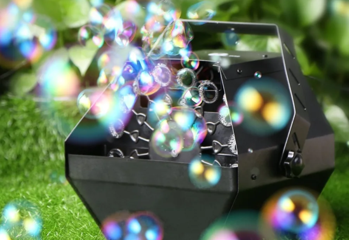 Black bubble machine blowing colorful bubbles on grass outdoors