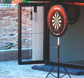Dartboard on a stand inside a room by an open glass door, with a brick wall visible outside.