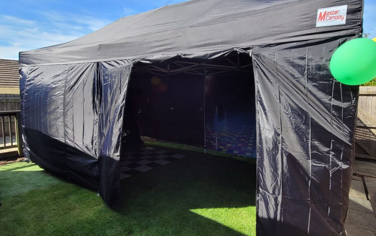 Black outdoor event tent with open front on grass, with a green balloon on the right