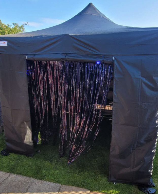 Black canopy tent with metallic fringe doorway on grass outdoors