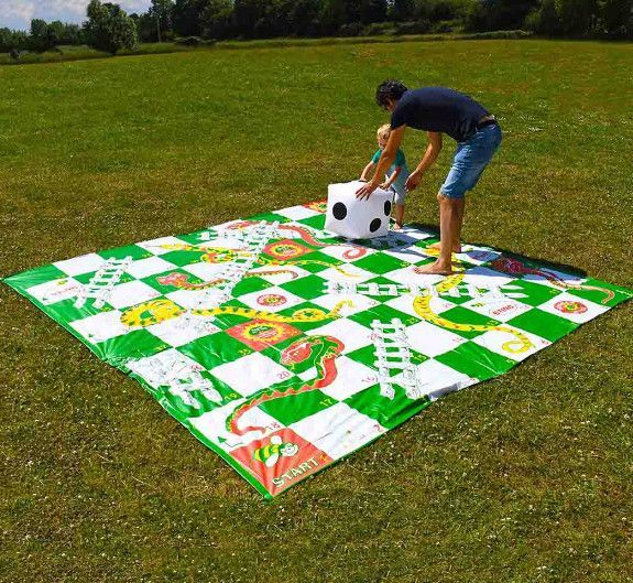 Person arranging a giant colorful checkered board game mat on grass outdoors