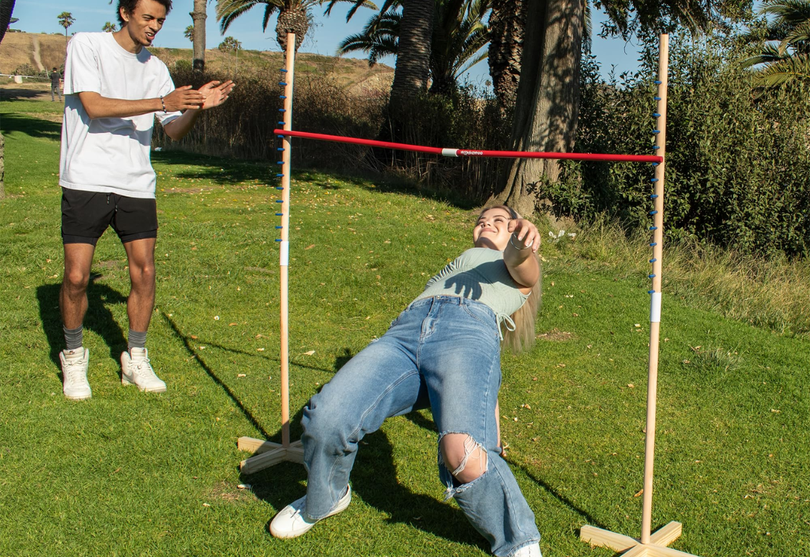 Two people outdoors during a limbo game, one leaning back under a red bar.