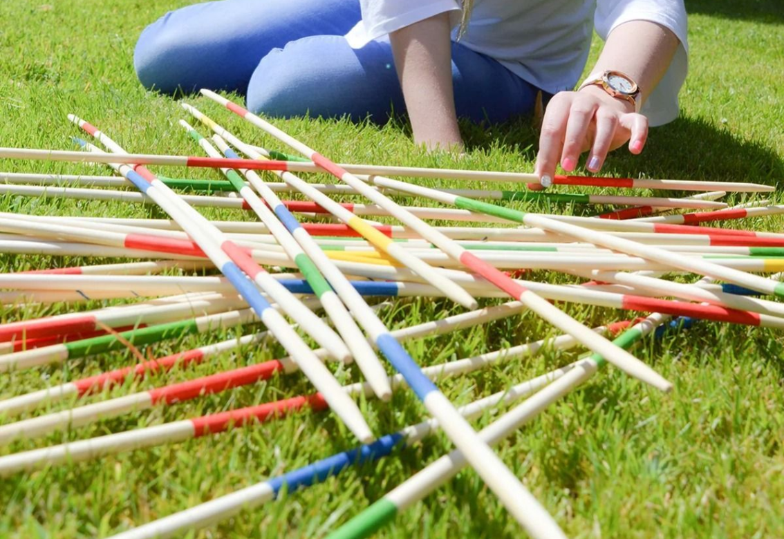 Colorful striped sticks scattered on green grass beside a person sitting outdoors