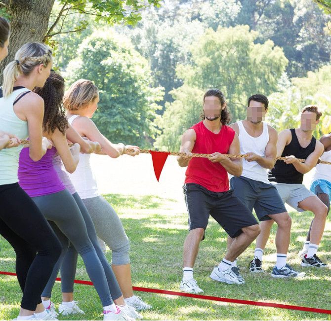 People in athletic clothes tugging a red rope during an outdoor team challenge in a park