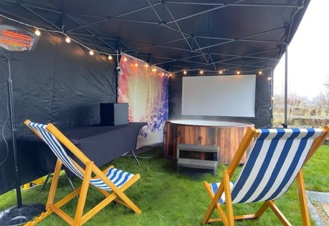 Outdoor movie setup with projector screen, black canopy, and blue-striped chairs on grass at sunset