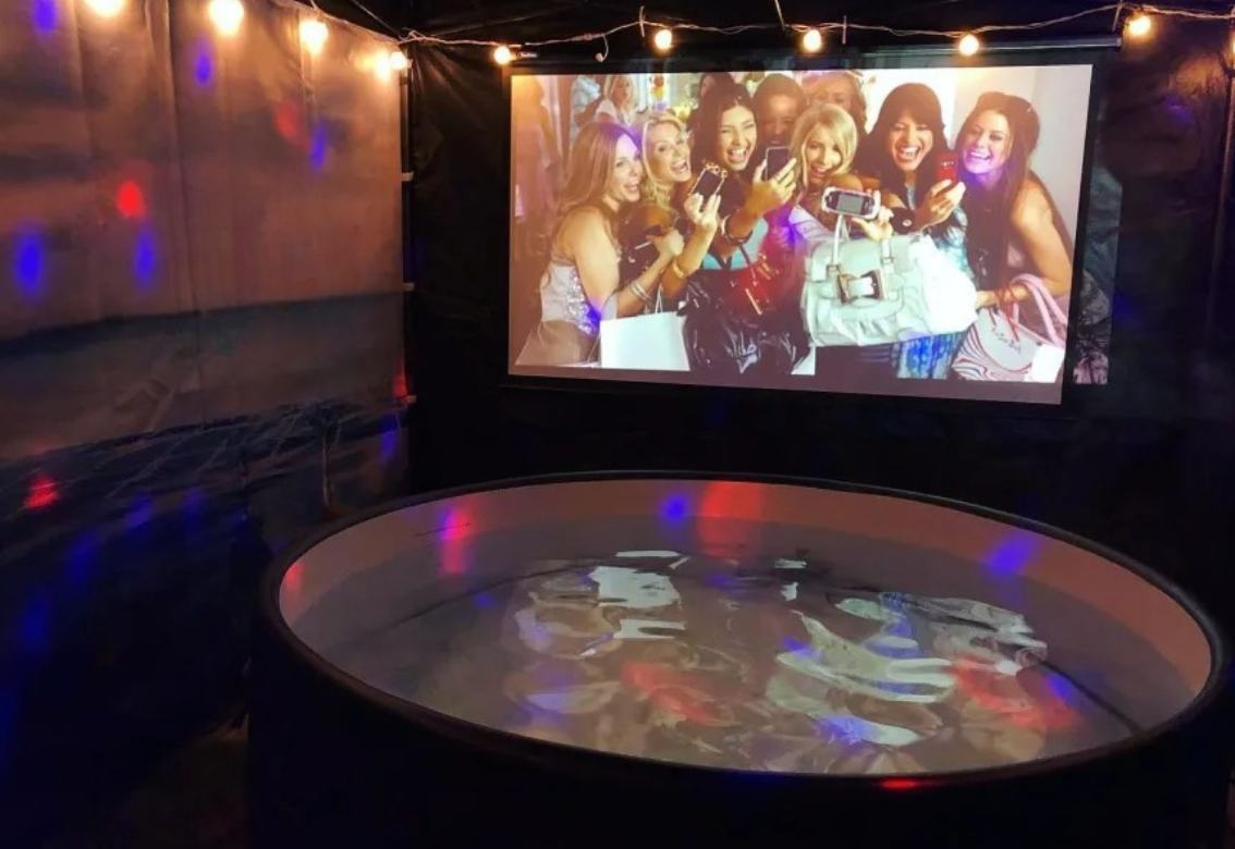 Dim karaoke booth with a glowing floor and a group photo projected on the wall