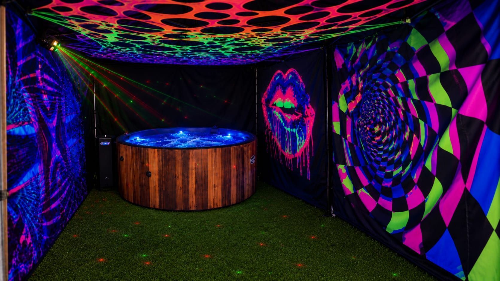 Round wood-fired hot tub in a grassy field, with hedges and countryside beyond.