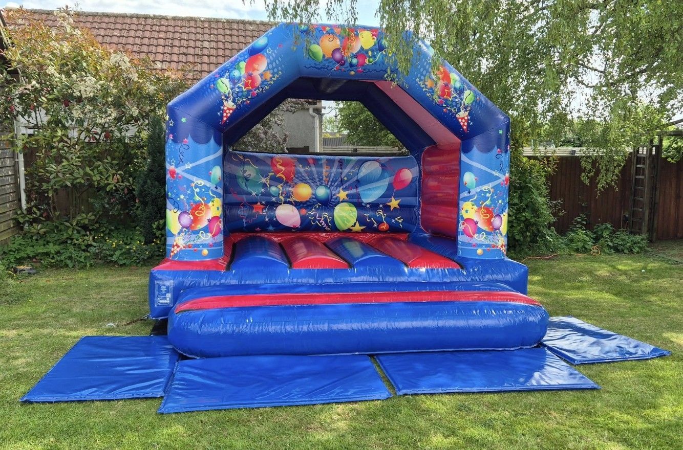 Blue space-themed inflatable bounce house on a grassy lawn with safety mats and no children present