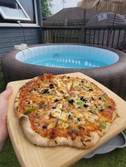 Hand holding a pizza peel with pizza in front of an above-ground backyard pool