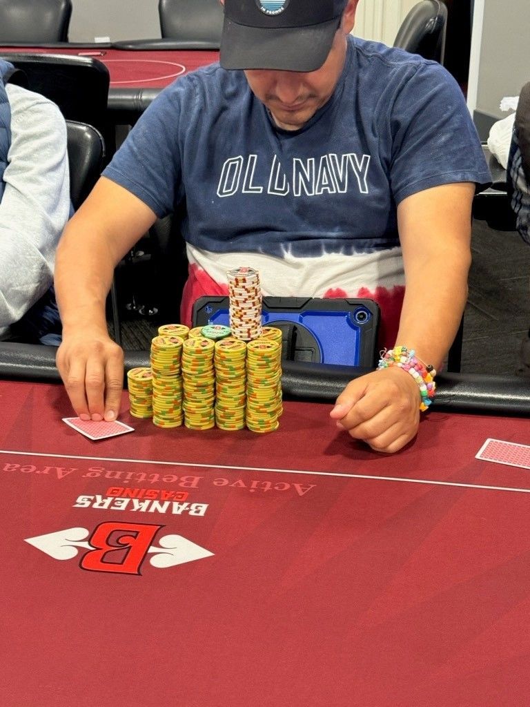 Poker player stacking yellow chips at a Banzai casino table, wearing a blue shirt and cap.