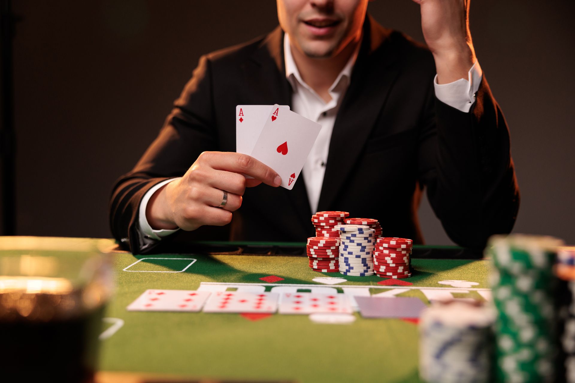 A poker player in a suit holding two aces beside stacked chips at a green felt table A poker player in a suit holding two aces beside stacked chips at a green felt table