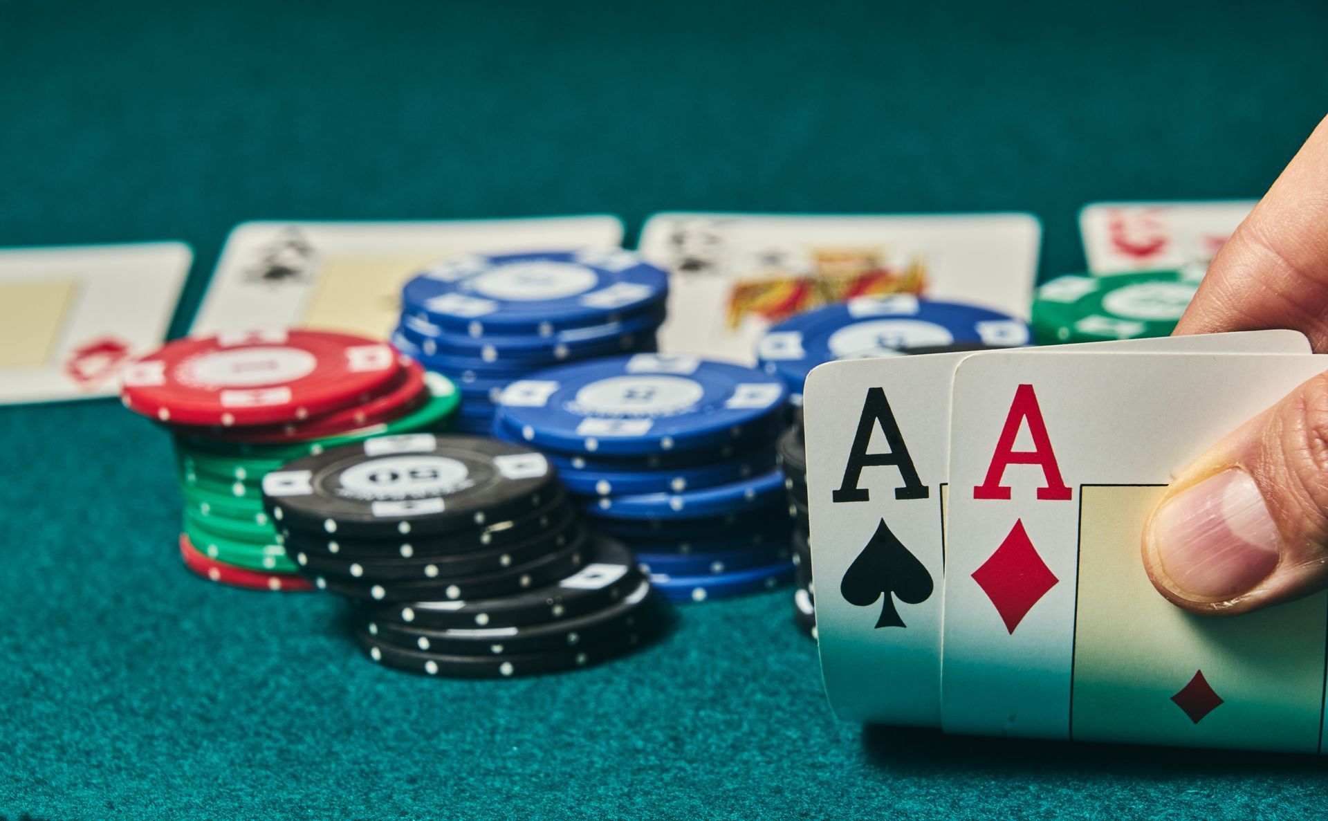 Close-up of a poker hand holding pocket aces with colorful chip stacks on a felt table.