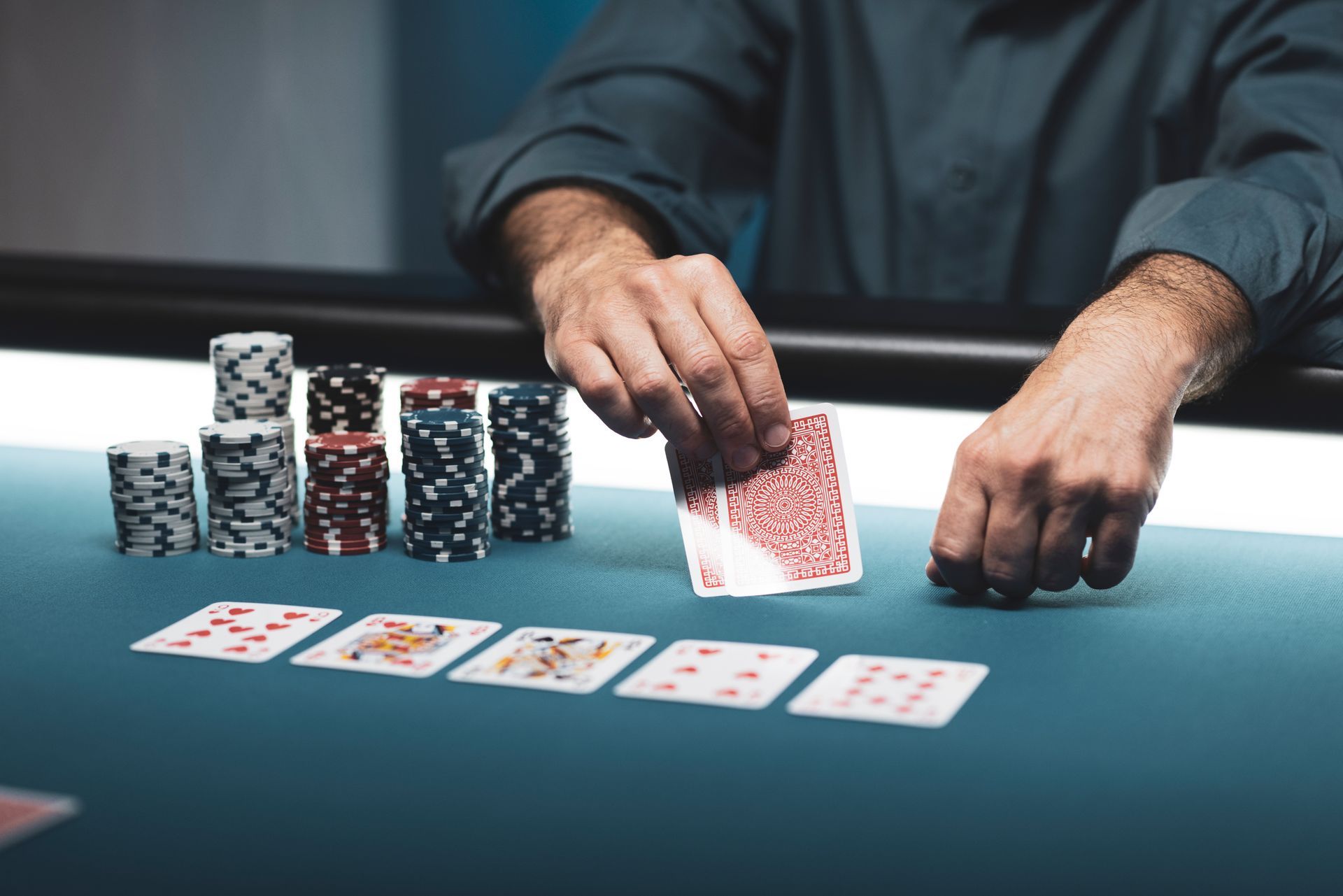 A poker player revealing a hole card beside stacked chips and five community cards on a felt table