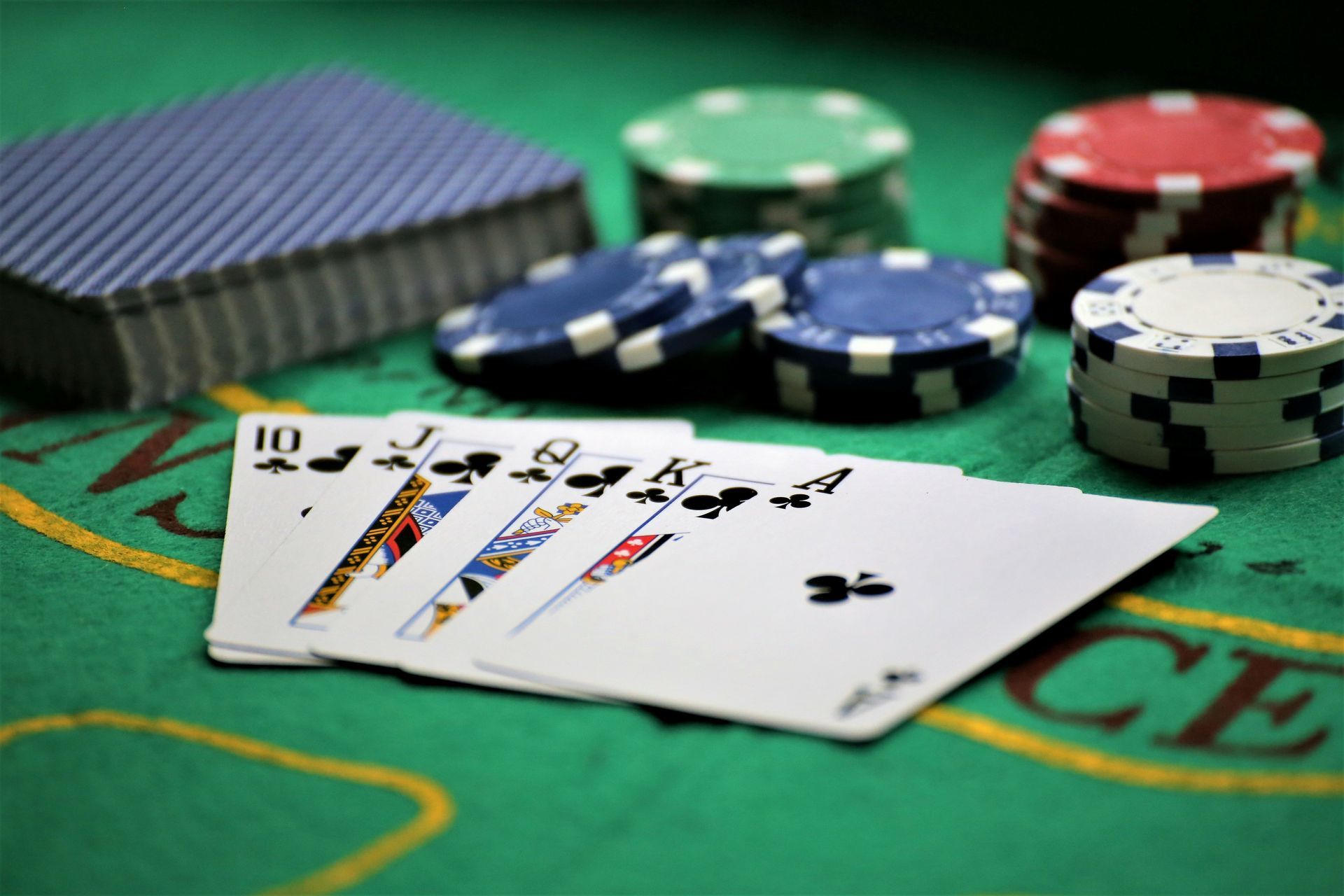 A poker hand with a royal flush in clubs on a casino table with playing cards and poker chips.
