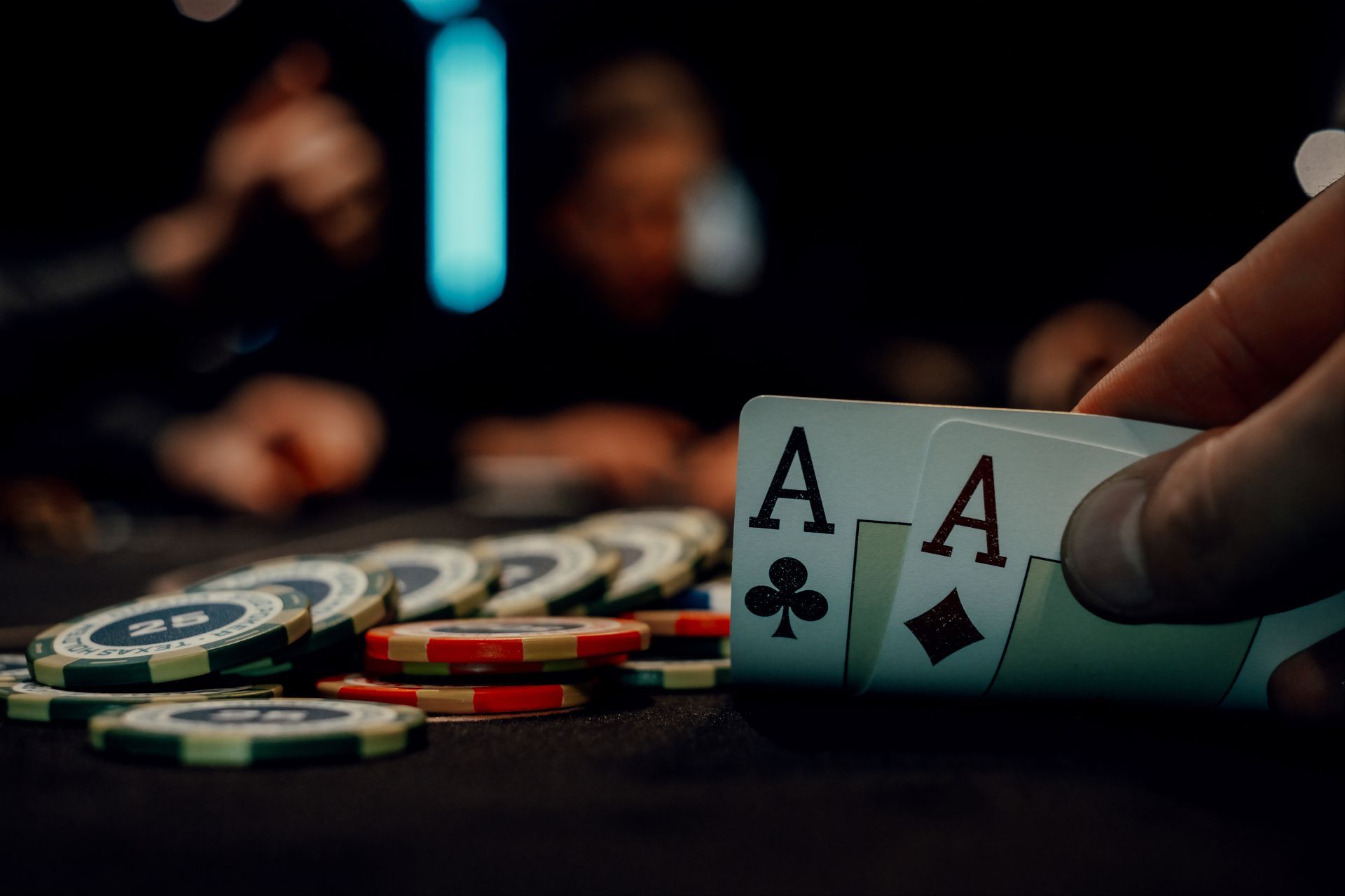 A player holds two aces over a table stacked with colorful poker chips. A player holds two aces over a table stacked with colorful poker chips.
