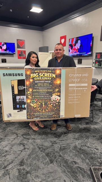 Two people holding a large TV box in an electronics store; a 
