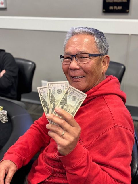 Smiling man in a red hoodie holding several dollar bills at a table in a meeting room