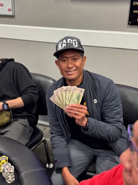 Man holding a fan of cash and smiling while seated on a black couch in a casual indoor lounge