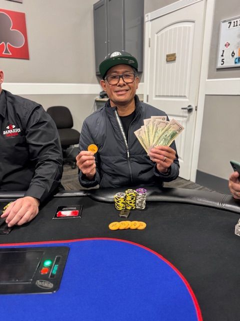 Man at a poker table holds cash and a chip, with cards and chips spread on the felt.