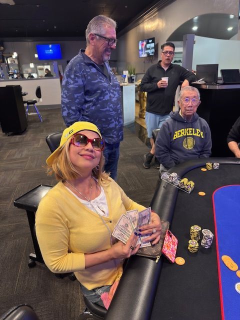 People at a casino table, with a woman in yellow smiling in the foreground holding cards.