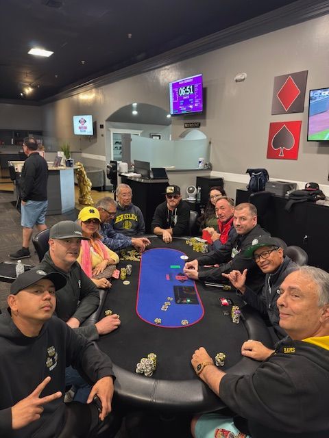 People seated around a poker table in a casino lounge, chatting and holding cards.