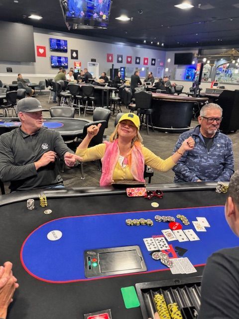 People seated at a poker table in a casino, with chips and cards on the blue felt table.