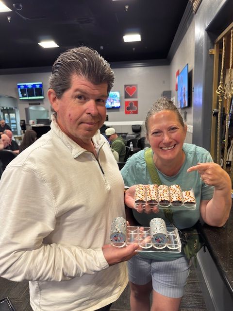 Two people in a bowling alley holding trays of decorated desserts and smiling at the camera.