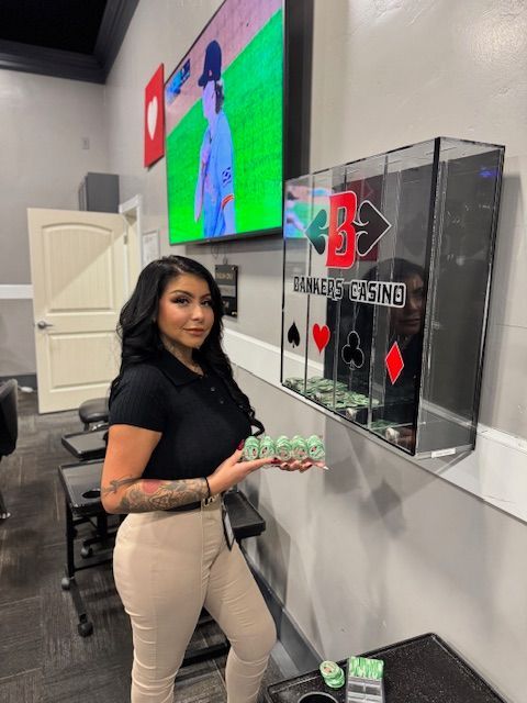 Woman standing indoors beside a display, holding green items, with a wall-mounted screen and acrylic sign behind her.