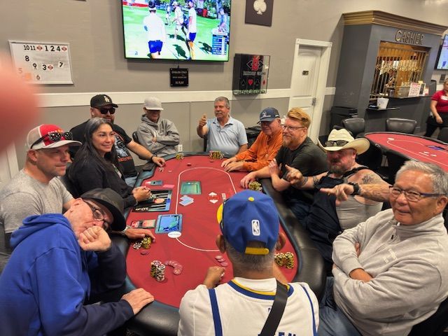 People playing poker around a red table in a casual room with a TV on the wall.
