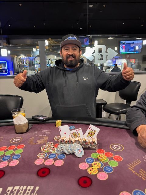 Man smiling at a poker table, giving thumbs up amid chips and cards in a casino-like room