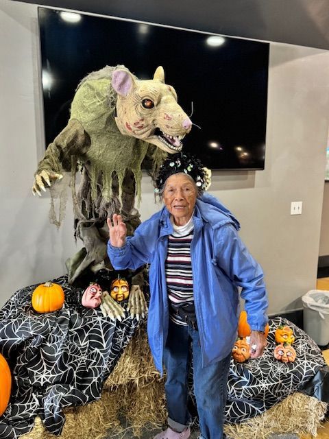 Person posing beside a large Halloween werewolf display with pumpkins and hay bales indoors