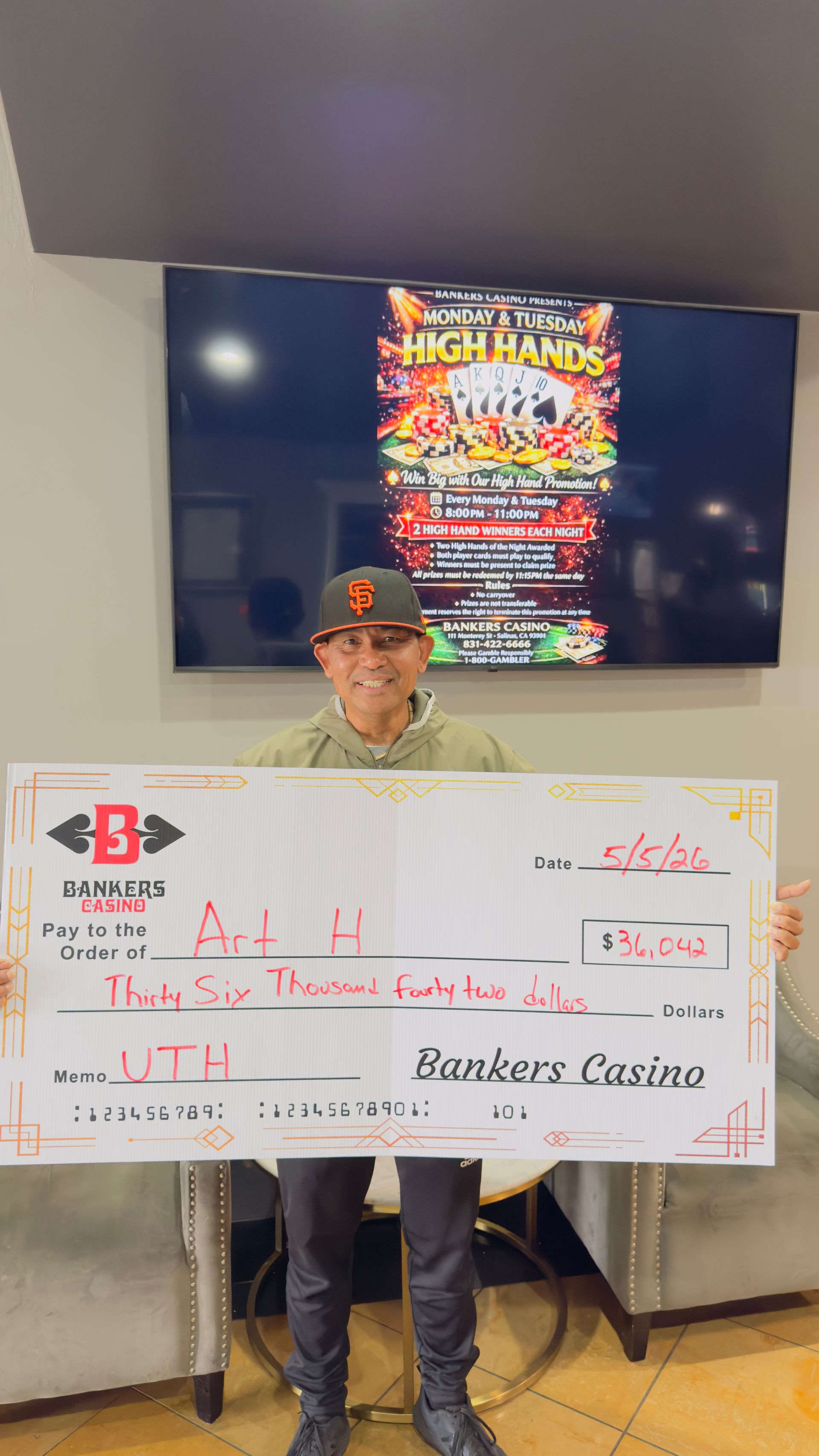 Person holding a large white check in front of a TV display at an event