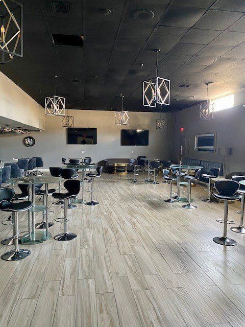 Empty modern lounge with high-top tables and stools, dark ceiling, and wood-look flooring