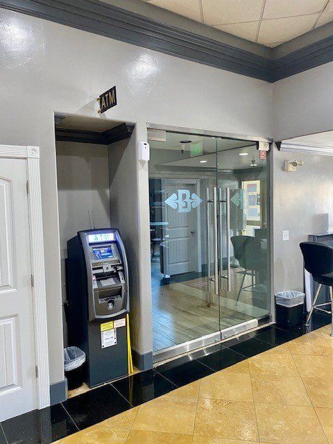 ATM beside glass office entrance in a lobby with tan tile floor and white walls