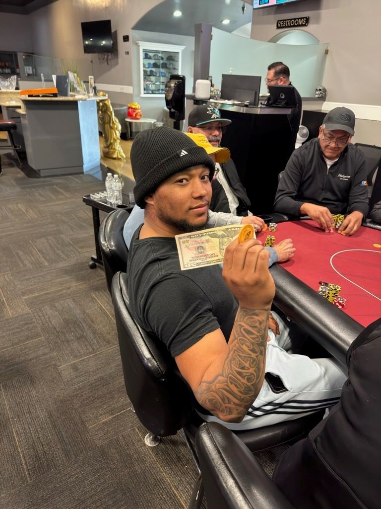 Man sitting at a poker table holding cash, with other players and chips in a casino lounge.