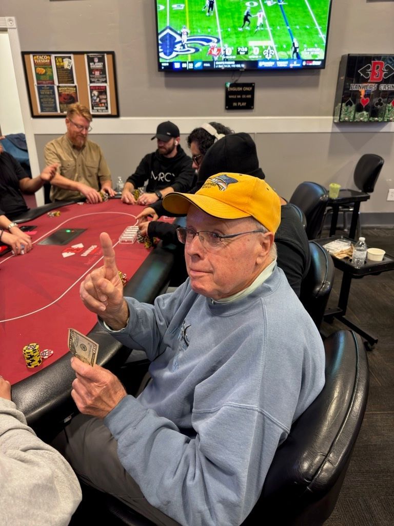 Man in yellow cap seated at a casino poker table, holding up two fingers with cards and chips nearby.