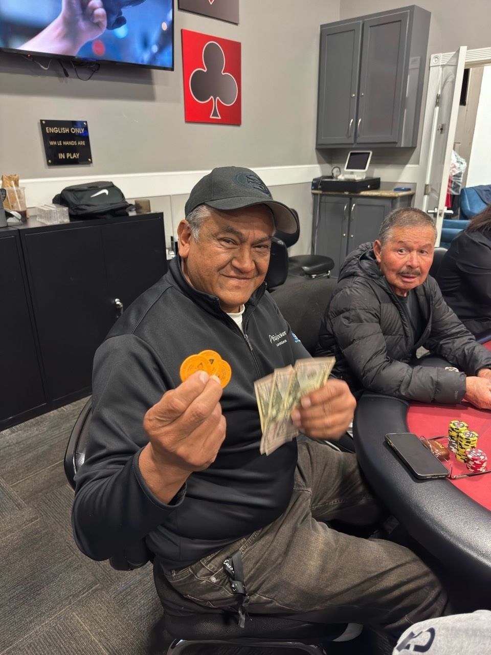 Man holding cash and an orange snack, smiling on a couch in a casual indoor lounge.