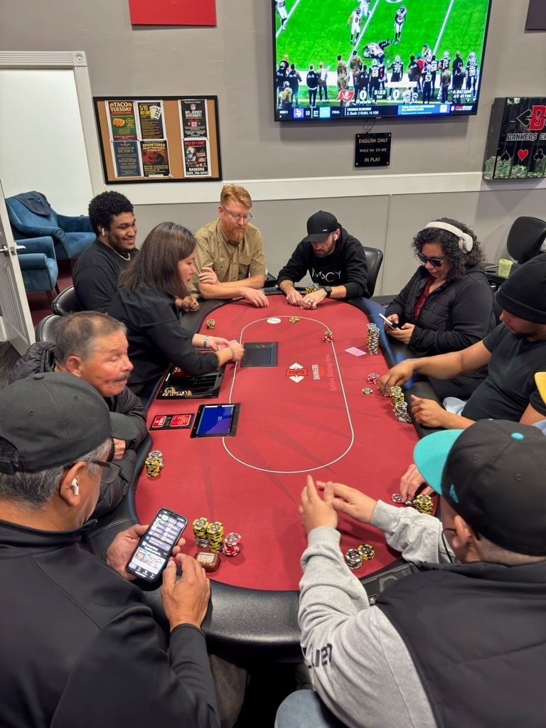 People seated around a red poker table in a lounge, watching a TV above them.