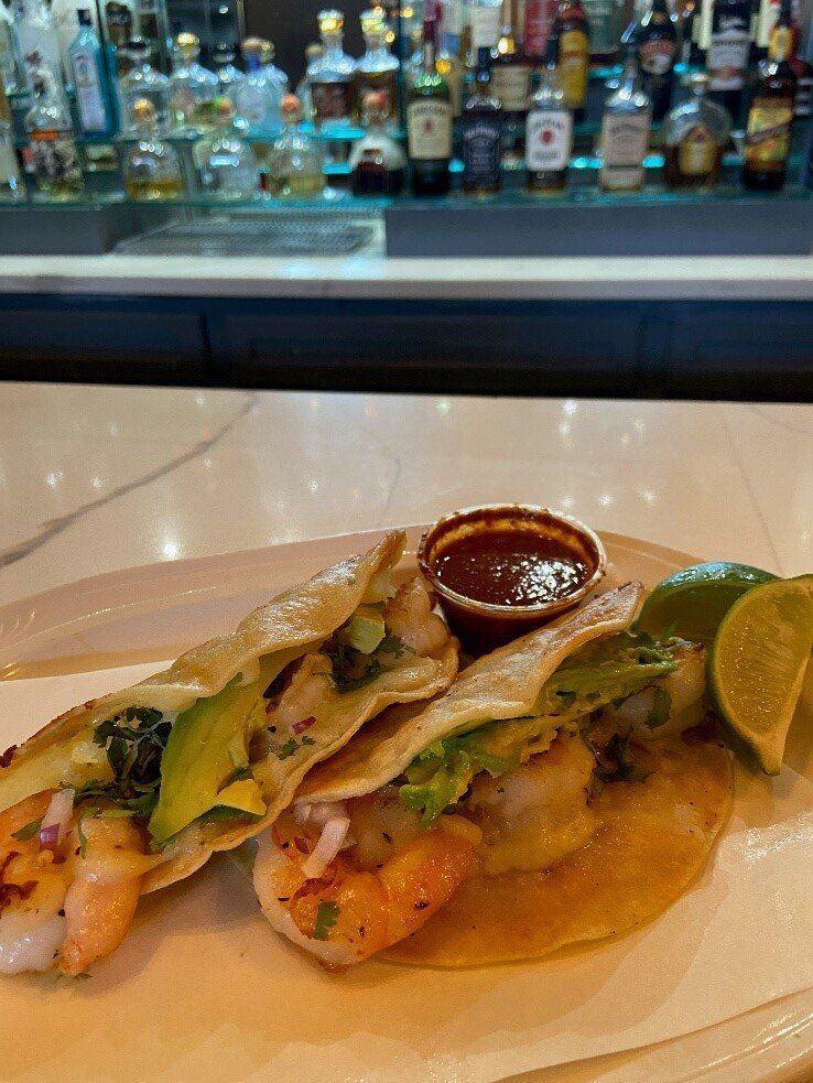 Tacos with lime and salsa on a white plate at a bar counter