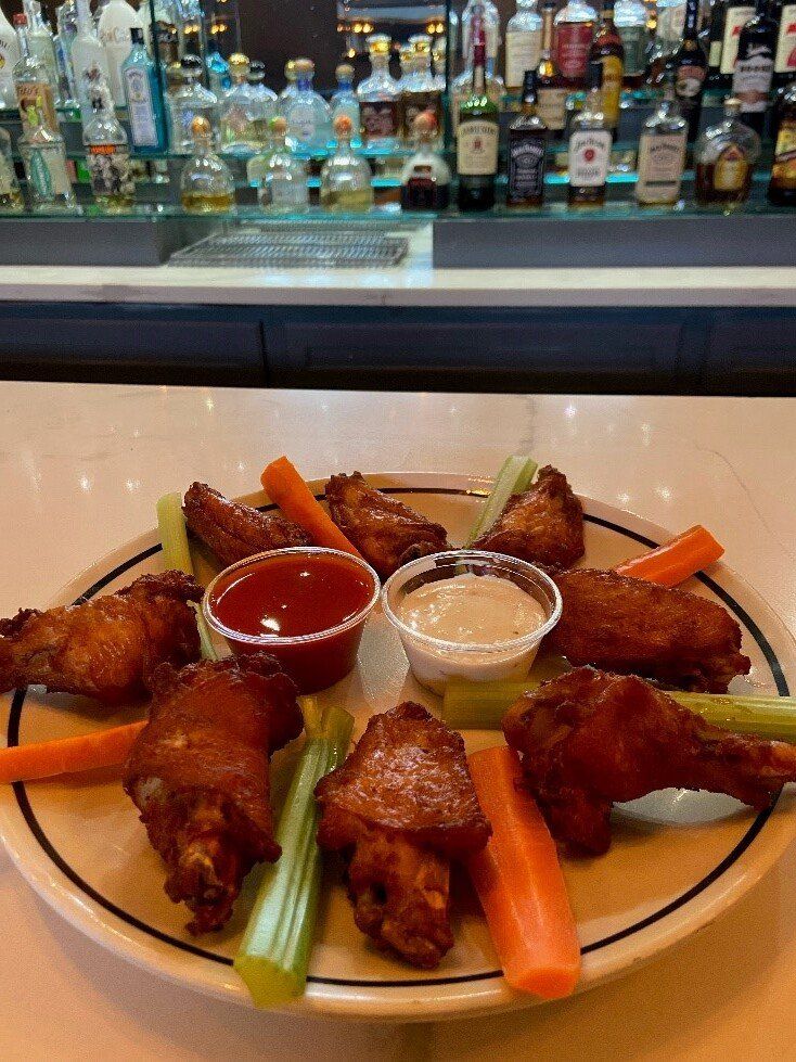 Buffalo wings with celery and dipping sauces on a plate at a bar counter