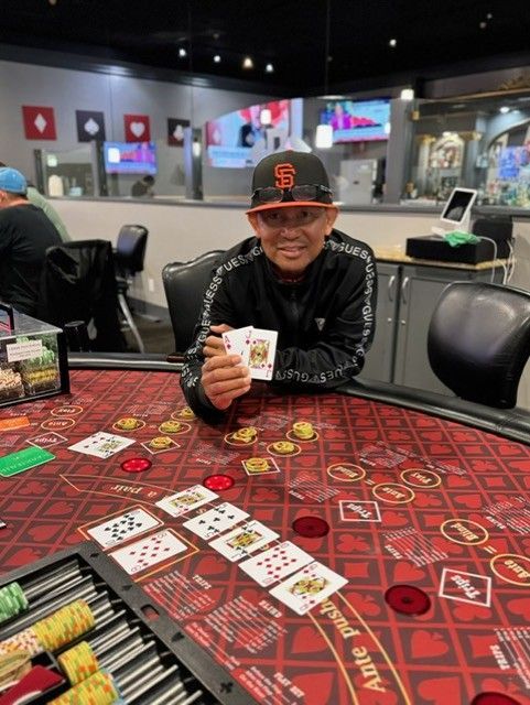 Person smiling at a casino table, holding cards and chips, with cards spread on a red felt layout.