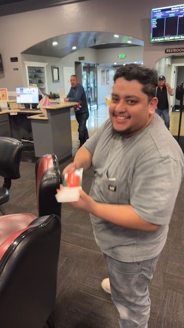 Man smiling in a gym lobby, holding a drink bottle and towel near cardio equipment.